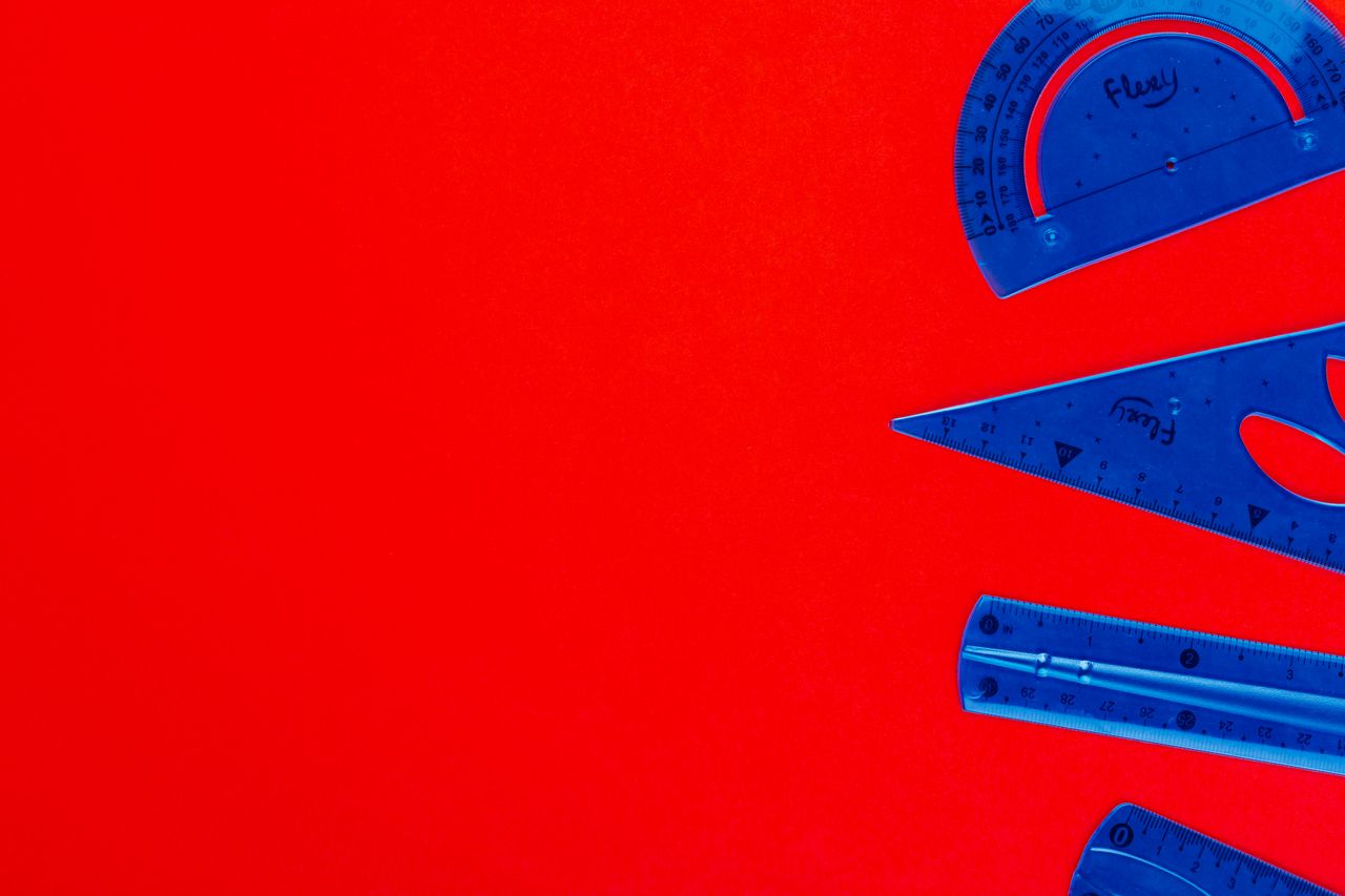 Blue plastic protractor, ruler, and set square on a vivid red background, perfect for educational themes.
