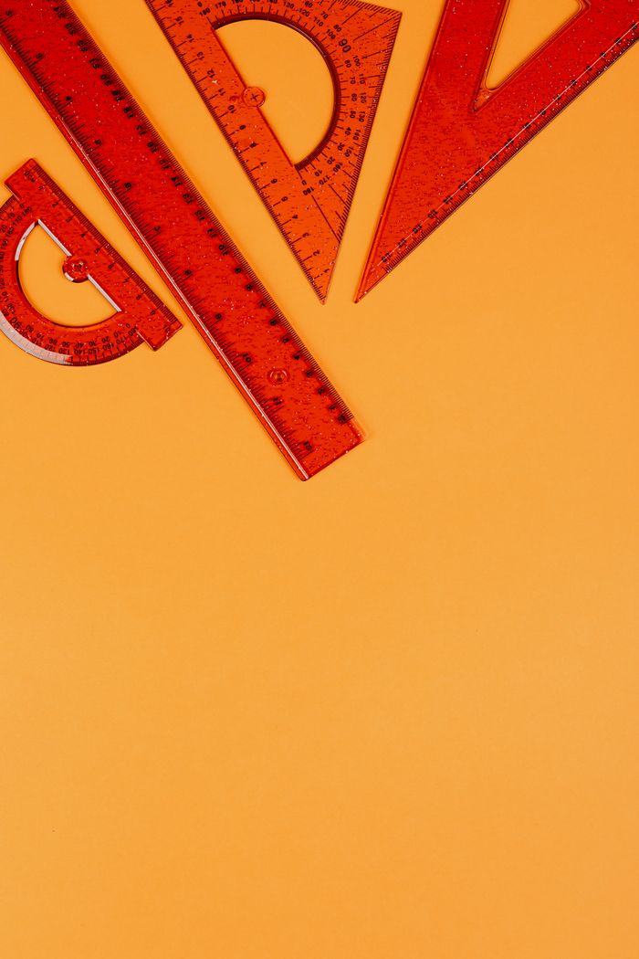 Top view of red rulers and protractors on an orange background, perfect for educational themes.