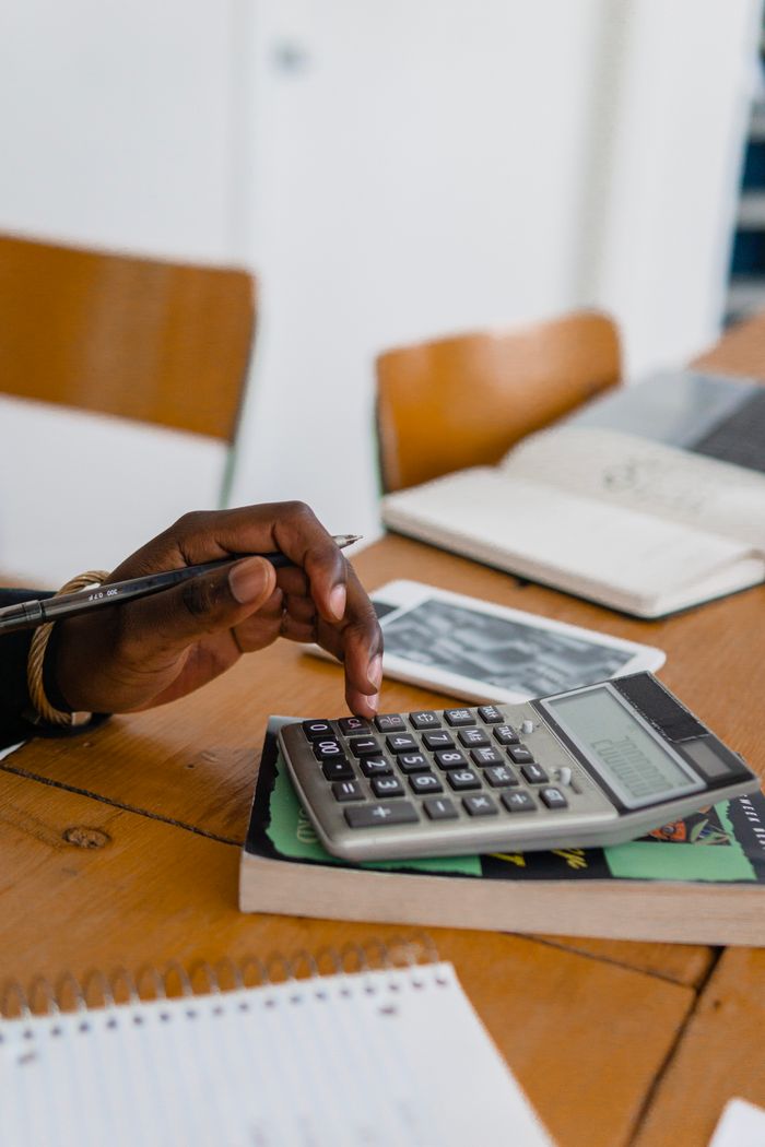 Services A person using a calculator on a wooden table, surrounded by books and stationery.